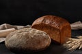 Variety of tasty baked bread sprinkled with flour and without it. Bunch of wheat, burlap, rolling pin, black background