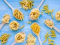 Variety of types and shapes of dry Italian pasta. Pasta ingredients on wooden spoons and blue background. Top view. Flat