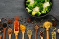 Various aromatic colorful spices and herbs in wooden spoons and scoops. Broccoli and cauliflower on iron frying pan. Top view