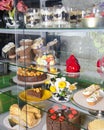 Various cakes with icing and desserts in refrigerated bakery case cabinet. Coconut shell dessert, chocolate cake.