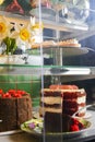 Various cakes with icing and desserts in refrigerated bakery case cabinet. Coconut shell dessert, chocolate cake.