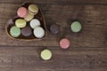 Various colored macaroons in a heart shaped wooden bowl isolated on a wooden background