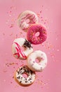 Various decorated doughnuts in motion falling on pink background