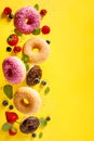 Various decorated doughnuts with sprinkles and berries in motion falling on yelloy background