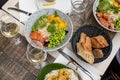 Various dishes and glasses with wine lying on table of French restaurant. Salads, bread arranged on plates on repast.