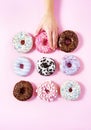 Various donuts on a pink background. A woman`s hand taking one. Royalty Free Stock Photo