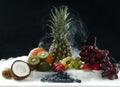 Various fresh fruits from coconut, pineapple, ripe, apples and grape on the white table in black background in smoke vapor