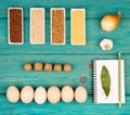 Various groats in bowls, eggs, bay leaf, onion, garlic, walnuts and notepad on blue table