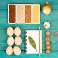 Various groats in bowls eggs, bay leaf, onion, garlic, walnuts and notepad on blue wooden table