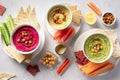 Various hummus dips in bowls, served with fresh vegetables and crisps.