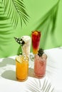 Various lemonade drink over green background. White table with sunlight and palm leaf hard shadow. Summer, tropical and juicy Royalty Free Stock Photo