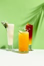 Various lemonade drink over green background. White table with sunlight and palm leaf hard shadow. Summer, tropical and juicy Royalty Free Stock Photo