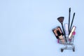 Various make-up products and brushes in shopping cart on blue background. Makeup cosmetics sale. Copy space Royalty Free Stock Photo