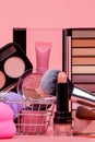 Various make-up products and brushes in shopping cart on pink background. Makeup cosmetics sale concept Royalty Free Stock Photo