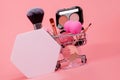Various make-up products and brushes in shopping cart on pink background. Makeup cosmetics sale concept Royalty Free Stock Photo