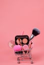 Various make-up products and brushes in shopping cart on pink background. Makeup cosmetics sale concept Royalty Free Stock Photo