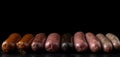 Various meat sausages lie in a row, black background, isolate. AI generated.