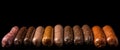 Various meat sausages lie in a row, black background, isolate. AI generated.