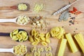 Various mix of pasta on wooden rustic background, wooden spoons, spices red pepper, bay leaf, diet and food concept, top view, set