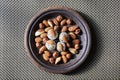 Various nuts are laid out in a brown handmade clay plate