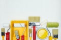 various paint brushes, rollers, paint cans and paint tray on white wooden background