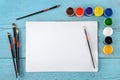 Various paints, brushes, white sheets paper on wooden blue background. Top view. Royalty Free Stock Photo