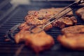Various pieces of meat are cooked on an iron cast grill for a BBQ - foreground with pliers blanked out blurry for copy space