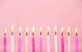 Various pink color birthday cake candles burning in line on pastel pink background. Royalty Free Stock Photo