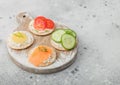 Various round healthy crackers with salmon and cheese, tomato and cucumber on wooden chopping board on light kitchen table Royalty Free Stock Photo