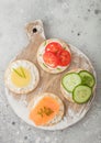 Various round healthy crackers with salmon and cheese, tomato and cucumber on wooden chopping board on light kitchen table Royalty Free Stock Photo