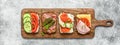 Various sandwich on a wooden board, gray concrete background. Open sandwiches with vegetables, bacon, salmon and ham