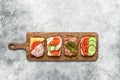 Various sandwich on a wooden board, gray concrete background. Open sandwiches with vegetables, bacon, salmon and ham