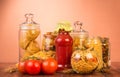 Various shapes pasta in jars, bottle ketchup, tomato on brown. Royalty Free Stock Photo