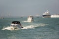 Various ships and boats sail along the huge sea bay. A distant factory with pipes can be seen on the horizon