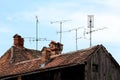 Various sizes TV antennas mounted on multiple metal poles on top of old dilapidated wooden house roof next to destroyed chimneys Royalty Free Stock Photo