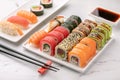 Various sushi rolls, soya sauce and chopsticks on a white stone background.