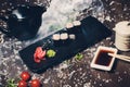 Various sushi on white plate with chopsticks on wooden background.