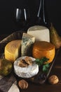 Various types of cheese with glass of wine on rustic wooden table. Dark background