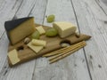 Various types of cheese, grapes, pistachios lie on a wooden triangular board.