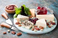 Various types of cheese on a wooden plate with jam, nuts and dried cranberries Royalty Free Stock Photo