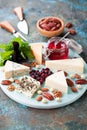 Various types of cheese on a wooden plate with jam, nuts and dried cranberries Royalty Free Stock Photo