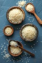 Various Types of Organic White Rice in Wooden Bowls and Spoons on Dark Textured Background