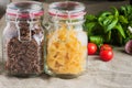 Various types of pasta, fusilli and farfalle, in glass jars next to tomato and garlic and basil