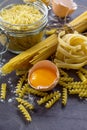 Various types of pasta spaghetti, fusilli, fettuccine and raw egg yolk on a kitchen wooden table. Royalty Free Stock Photo