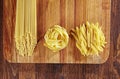 Various types of pasta on wooden table with cutting board, top view. Pappardelle, spaghetti, Penne pasta on dark wood