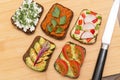 Various vegan, vegetarian healthy toasts on wooden board on kitchen with different vegetables, top view