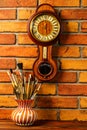 Vase with artistic brushes and old wooden wall clock with barometer and thermometer on the brick wall background Royalty Free Stock Photo