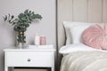 Vase with beautiful eucalyptus branches, book and candles on nightstand in bedroom