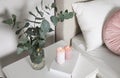 Vase with beautiful eucalyptus branches, book and candles on nightstand in bedroom