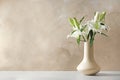 Vase with beautiful lilies on table against light brown background, space for